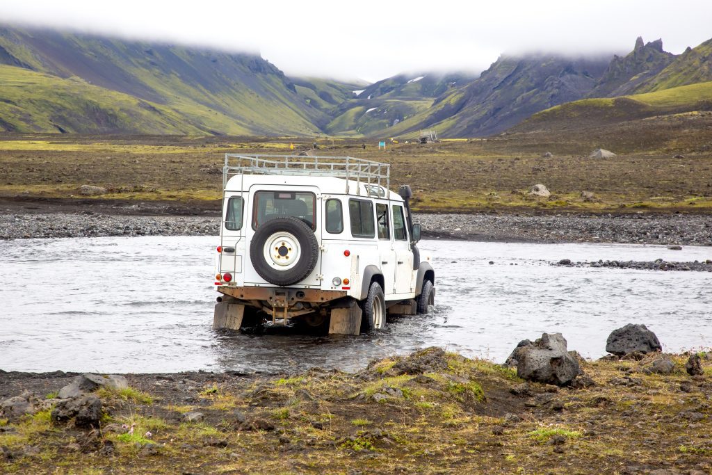 Crossing a tourist jeep car across a mountain river on the road. Stormy mountain river flows from glaciers in Iceland